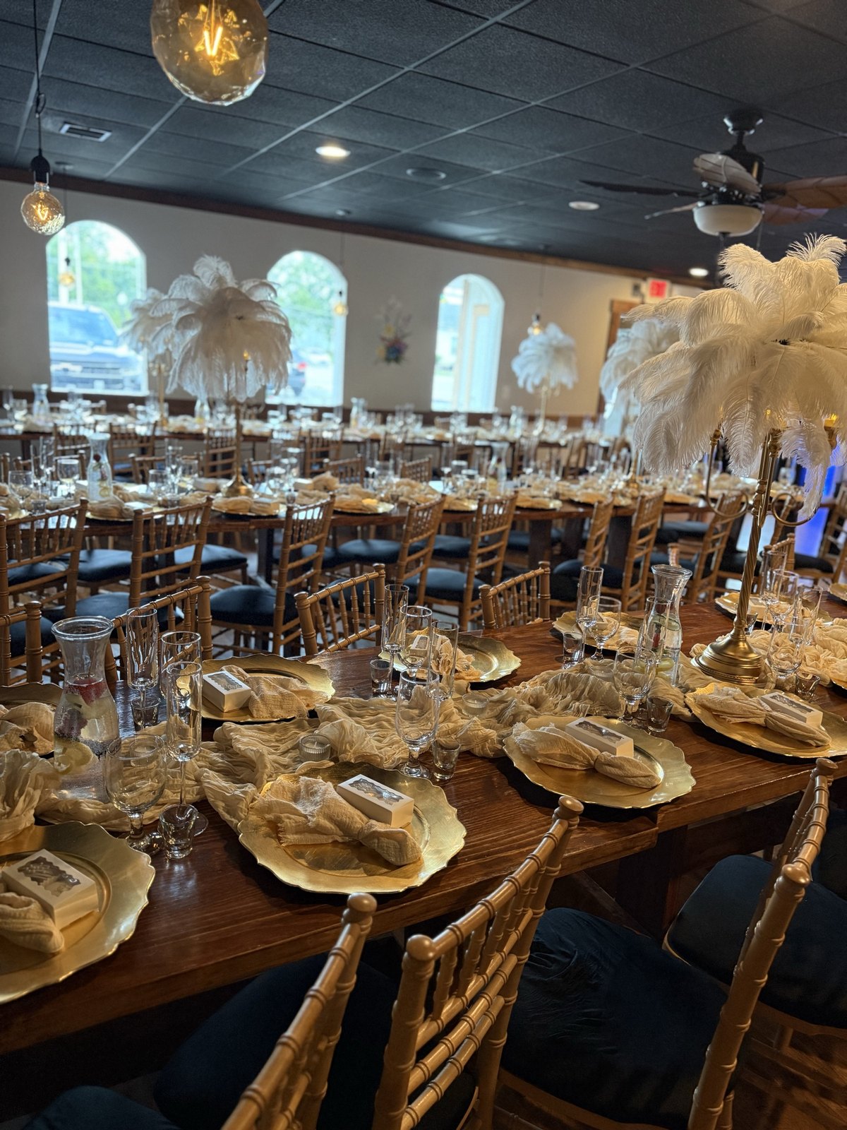 Banquet tables set with gold chargers and feather centerpieces