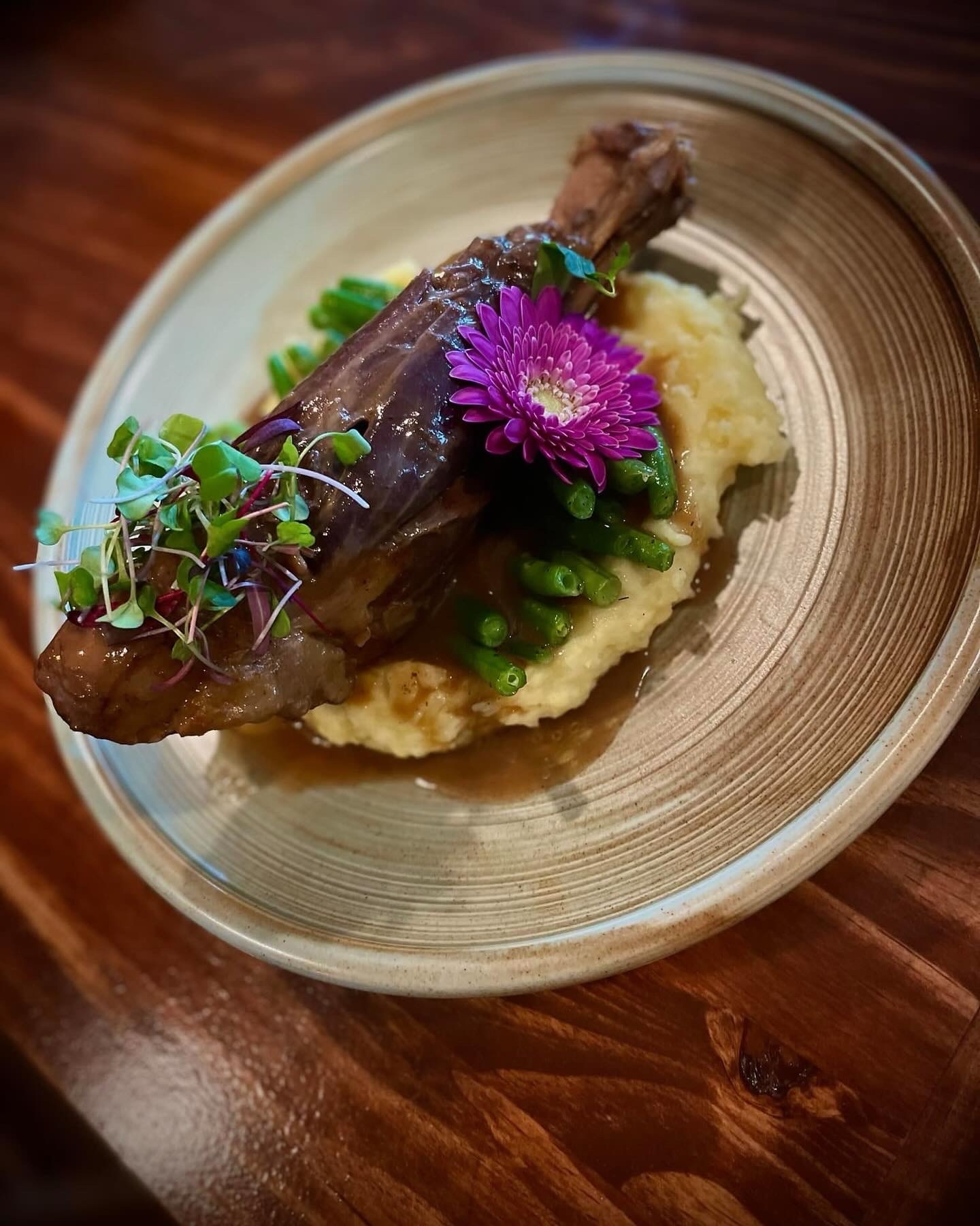 Roasted lamb shank with green beans and herb gravy on a stone plate by the fireplace