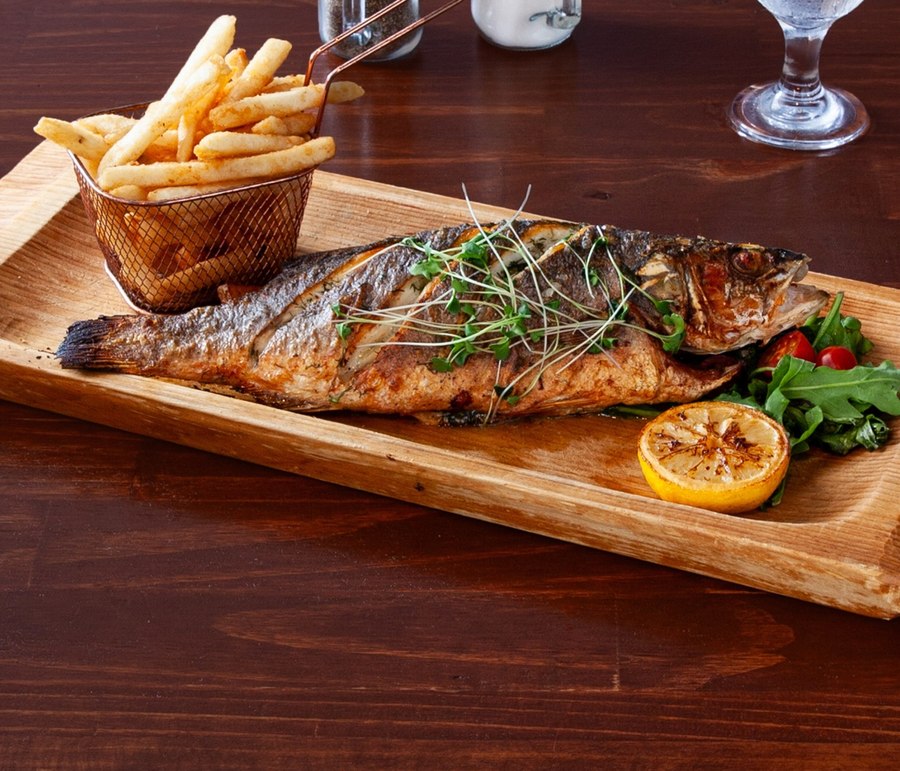 Whole baked rainbow trout with fries, grilled lemon and arugula on a wooden board